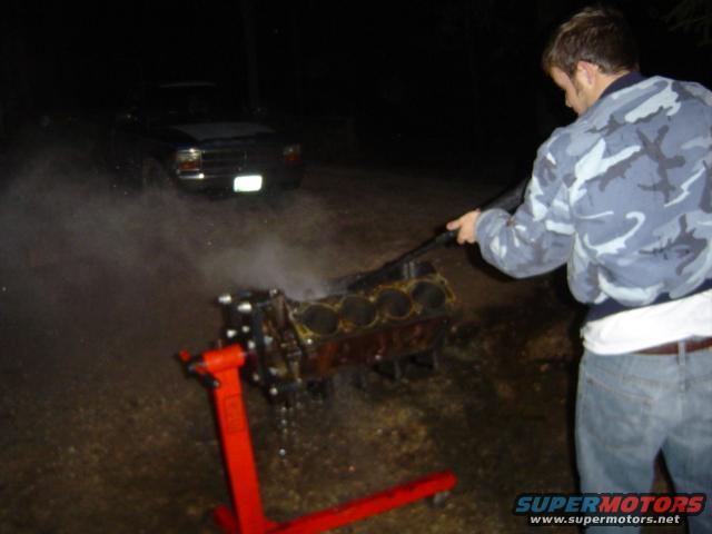 Man cleaning engine block on red stand; truck in background