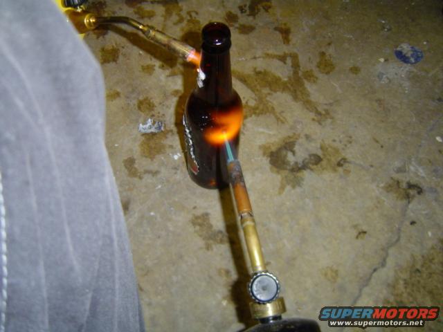 Brown glass bottle being heated by a torch on a concrete floor