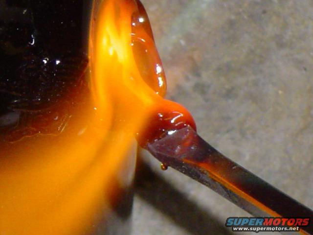 Molten orange glass drips from a tool onto a dark surface. Supermotors.net logo visible