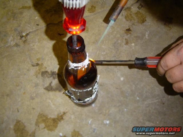 Someone is heating a bottle with a screwdriver and a soldering iron