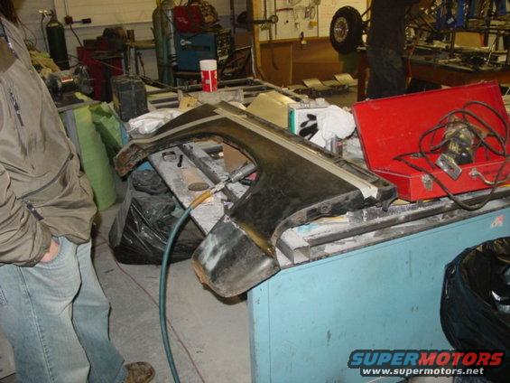 Car fender resting on a blue workbench in a garage, with tools and equipment in the background