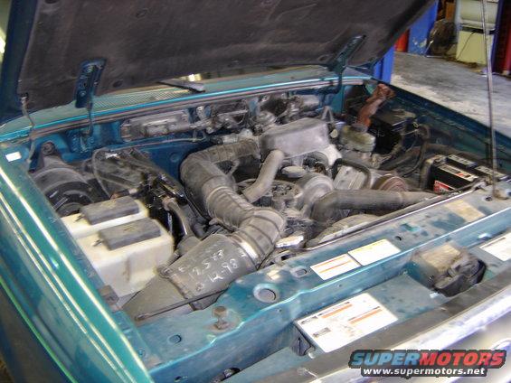 Engine bay of a teal Ford Ranger, showing engine components and some handwritten notes on a hose