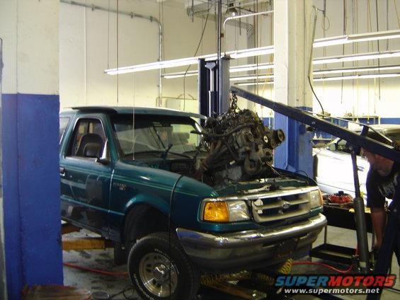 Green Ford Ranger on lift, engine being removed by crane. Front view