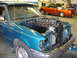 1997 Ford Ranger - A teal 1997 Ford Ranger is shown with its engine removed, revealing the engine bay, while a red Ford F-150 is parked in the background.