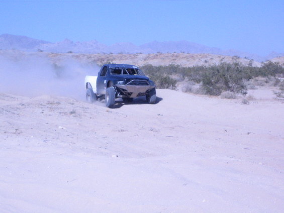 Black and white off-road truck kicking up dust on a dirt track, front bumper visible