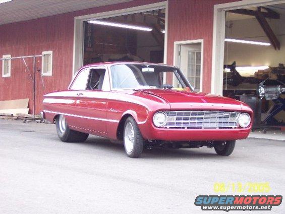 Red 1960 Ford Falcon coupe hot rod parked in front of a red garage