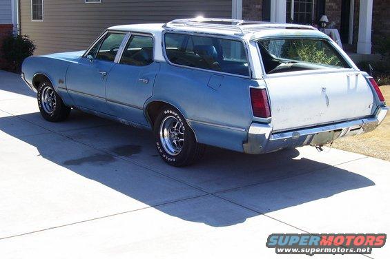 Blue and white 1970 Oldsmobile Cutlass station wagon, rear 3/4 view, chrome wheels, roof rack
