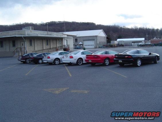 Several cars parked in a lot, including a red Chevrolet Camaro and a black Chevrolet Camaro