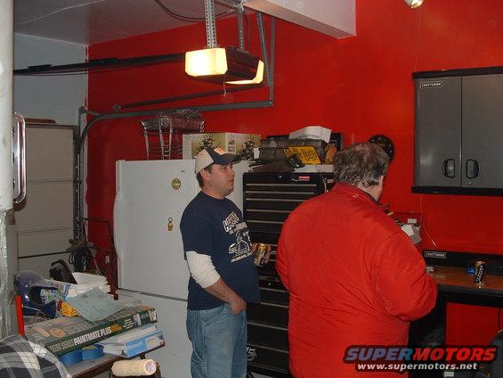 Garage interior with two men, tool chests, and a refrigerator