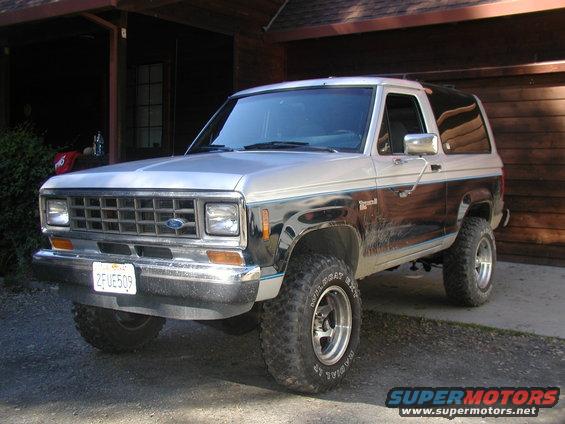 1987 Ford Bronco II parked in front of a wooden garage, showing front 3/4 view