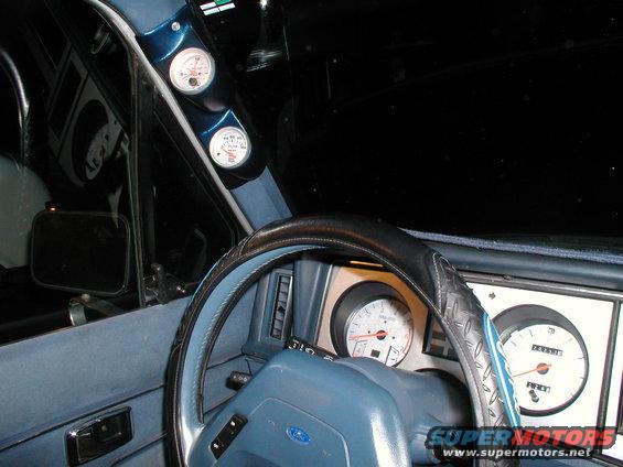 Blue dashboard of a 1987 Ford Bronco II with a steering wheel, tachometer, speedometer, and two auxiliary gauges