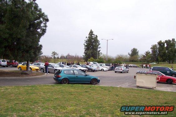 Teal hatchback car parked in a lot with other vehicles and trees
