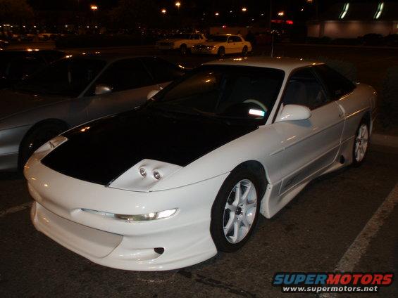 White Ford Probe with black hood, custom body kit, and white rims, parked at night