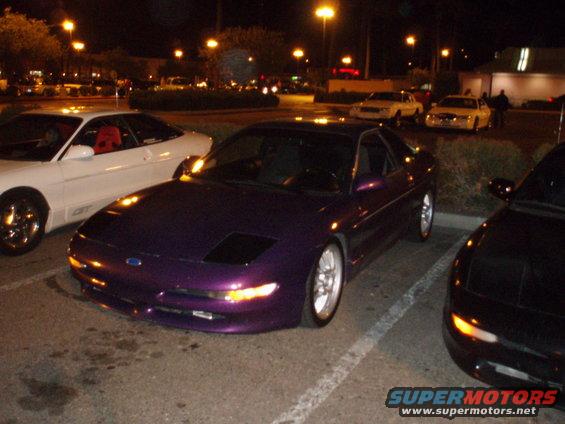Purple sports car parked at night, front 3/4 view. Aftermarket wheels and lowered suspension are visible