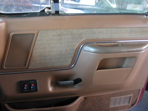 Brown car door panel with textured fabric insert, chrome trim, and a pull handle