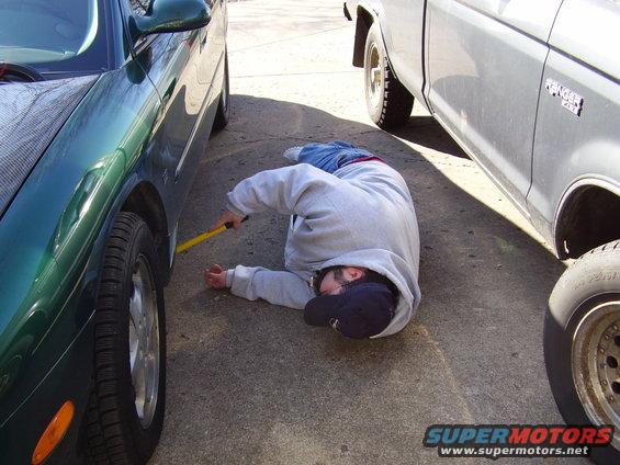 Person lying on ground between green car and silver pickup truck