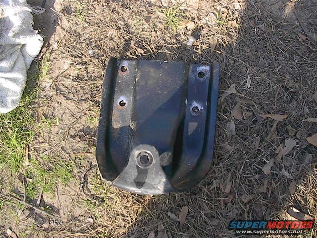 Black metal part with bolt holes and a circular opening, lying on the ground