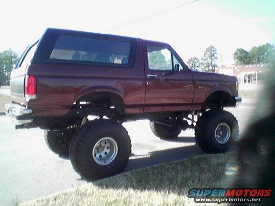 Maroon lifted Ford Bronco with large off-road tires, side view
