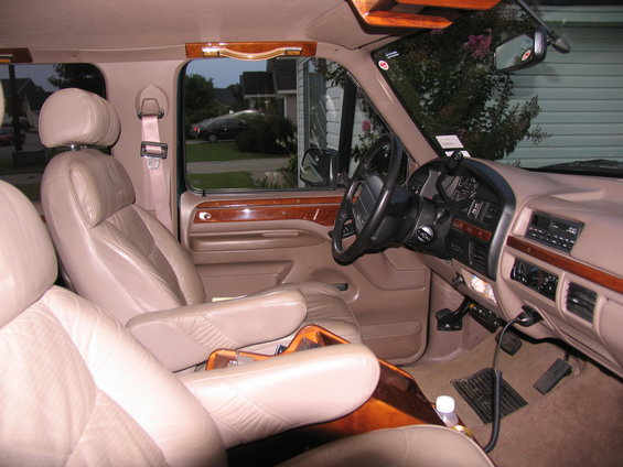 Tan leather captain's chairs and wood trim interior of a van, viewed from passenger side