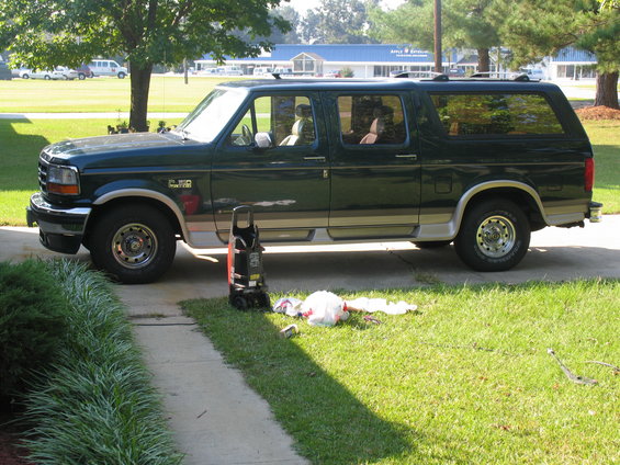 Green extended Ford SUV parked on driveway, pressure washer and cleaning supplies on lawn