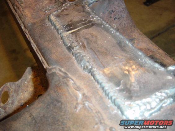 Close-up of heavily welded, rusty metal frame section with visible weld beads