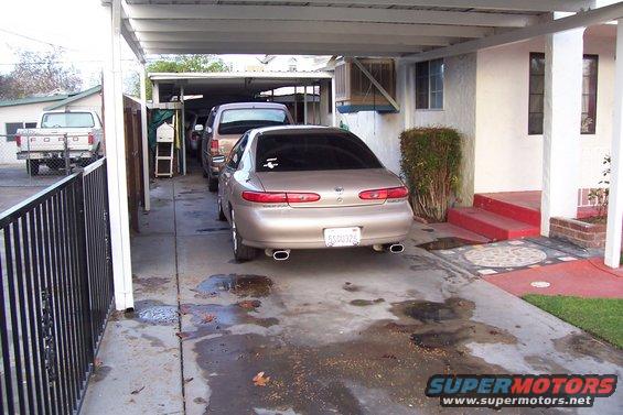 gold sedan parked in driveway, another vehicle and a truck visible