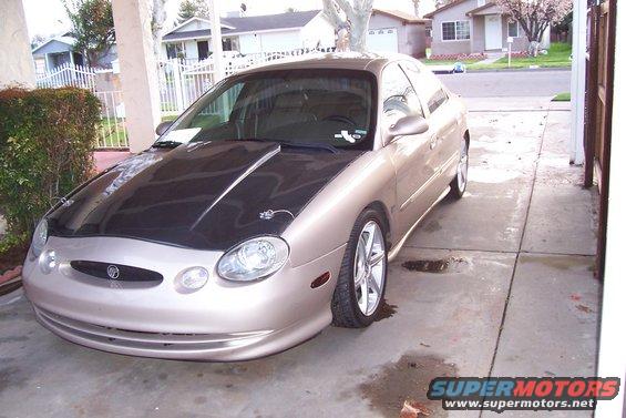 Gold sedan with a black hood, modified front bumper, and aftermarket wheels parked in a driveway