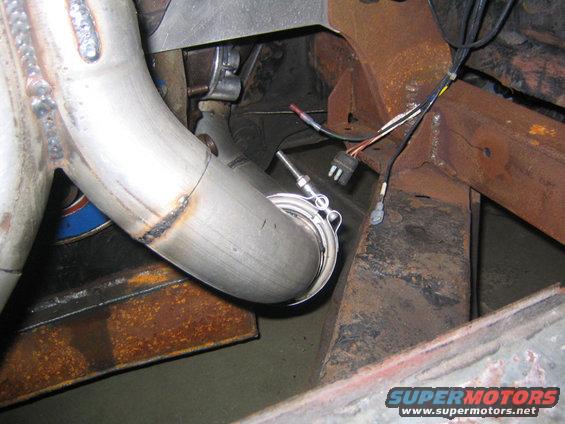 Close-up of an exhaust pipe with a sensor attached, showing welds and rusty metal frame