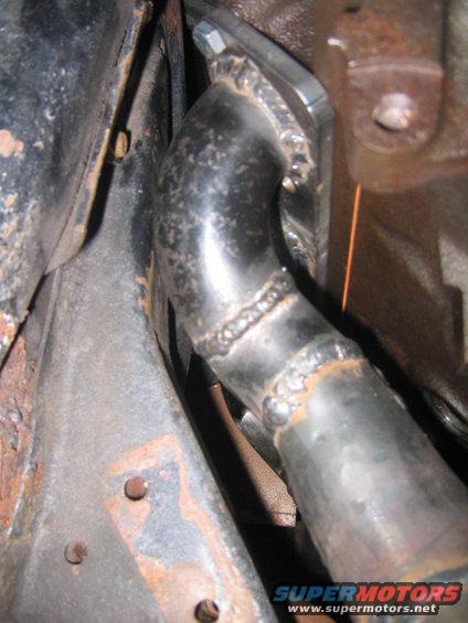 Close-up of a welded exhaust pipe connection with visible rust on surrounding metal components