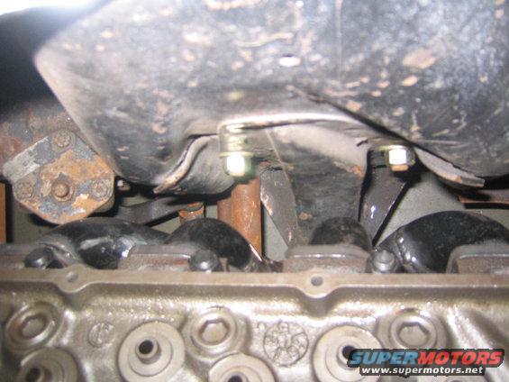 Close-up of an engine block with the oil pan above it. Bolts and rusty metal parts are visible