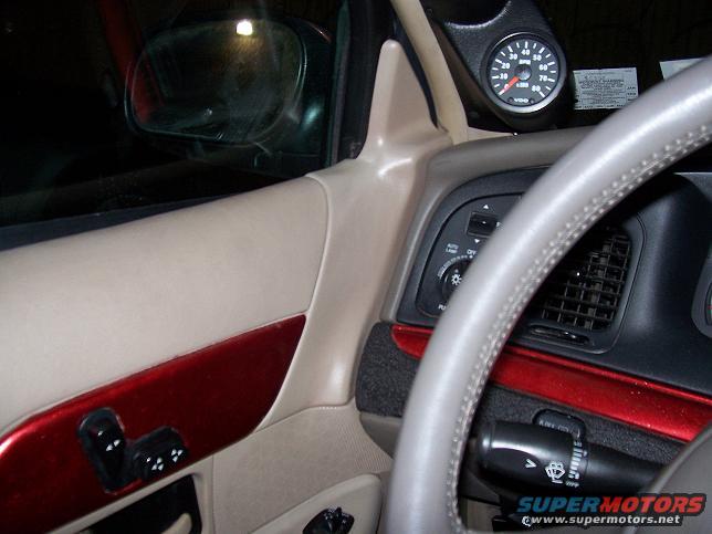 Car interior with beige door panel, red trim, and steering wheel. Aftermarket gauge mounted on dashboard