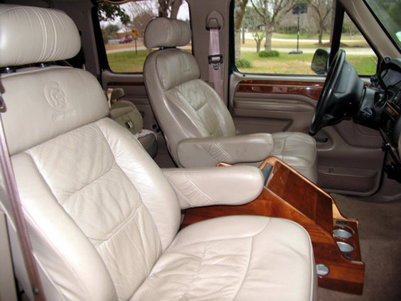 Interior of a van with tan leather seats and wood trim console. Centurion logo on headrest