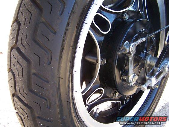Close-up of a motorcycle's rear wheel, showing the tire tread and black rim with white accents