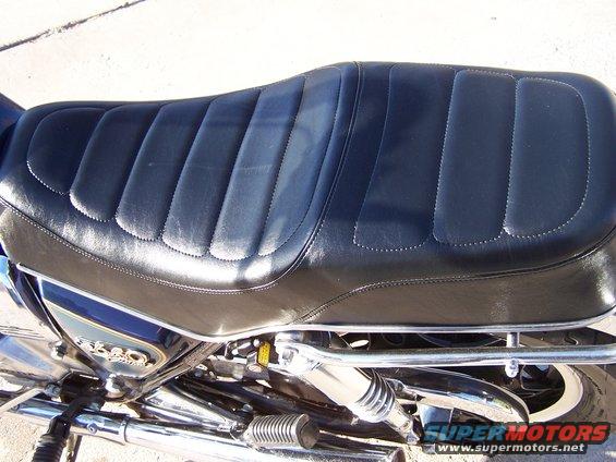 Close-up of a black motorcycle seat with ribbed padding. A badge on the side reads 'CB750'
