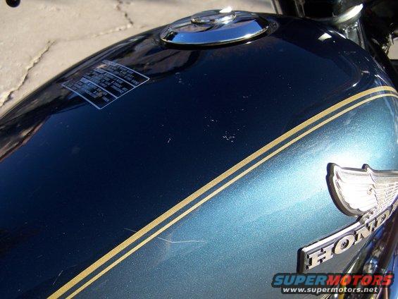 Dark blue motorcycle fuel tank with gold pinstripes and a chrome Honda emblem