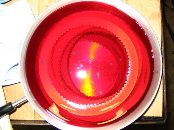 Clutch pack soaking in red transmission fluid inside a metal pan. Some text is visible on one of the clutch plates