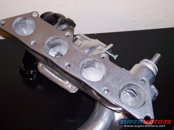 Aluminum turbo manifold with four intake ports and a black actuator. Visible text: SUPERMOTORS.NET