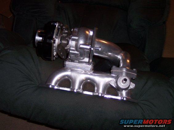 Turbocharger with black wastegate actuator attached to a polished exhaust manifold, resting on a dark green fabric surface