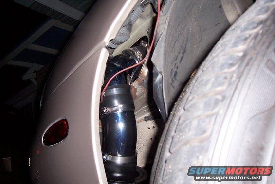Close-up of a black cold air intake tube with silver hose clamps, installed near a car's tire
