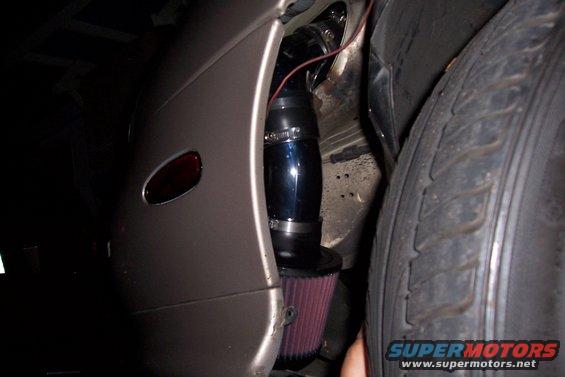 close-up of aftermarket cold air intake with red filter next to tire and fender