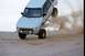 1985 Ford Bronco II - A white SUV performs a jump over sand dunes, its tires kicking up a cloud of dust.