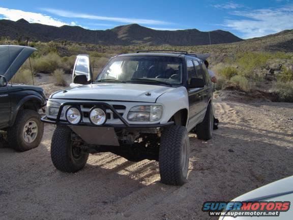 Modified white SUV with aftermarket bumper and lights parked off-road