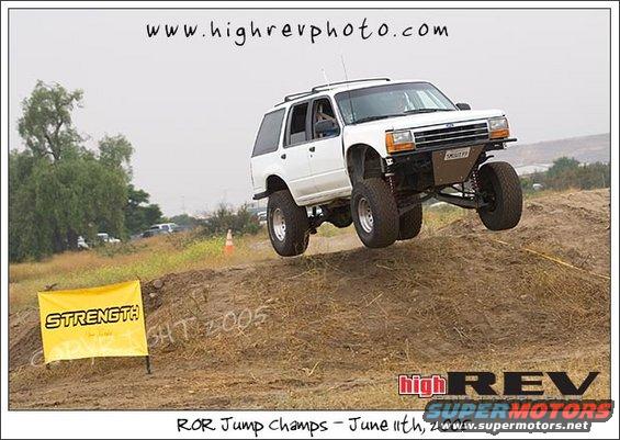 White SUV with lifted suspension and large tires airborne over a dirt jump