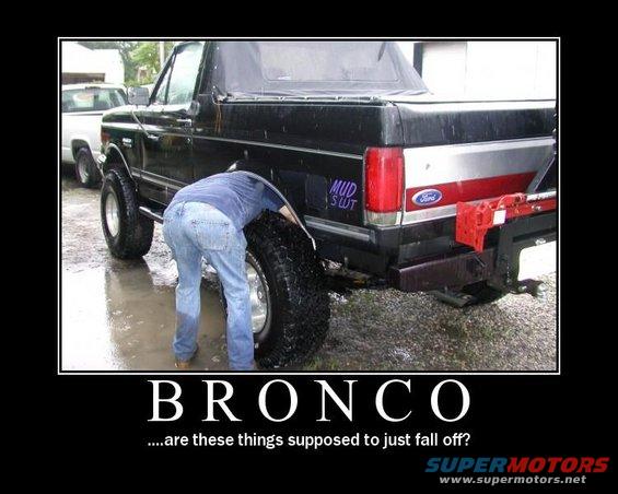 Person checking a tire on a black Ford Bronco. Another white truck is parked behind it