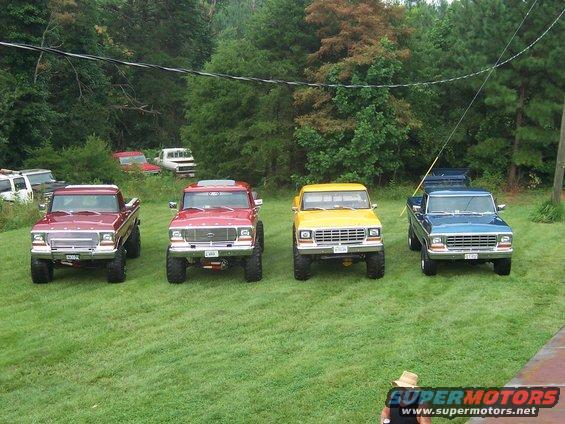 Four lifted Ford trucks parked on grass, two red, one yellow, one blue