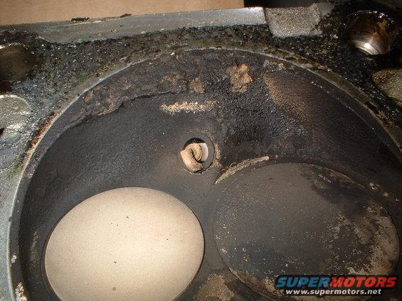 Engine cylinder head with carbon buildup and two valve openings. Watermark reads SUPERMOTORS.NET