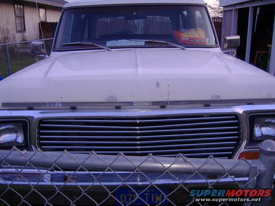 Front view of a white Ford F-Series truck, possibly a 1979 model, behind a chain-link fence
