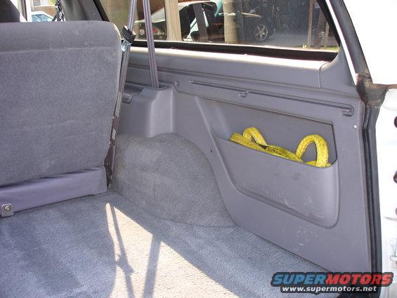 Interior cargo area of a 1996 Ford Bronco showing grey carpet, a side storage pocket with a yellow tow strap, and a seatbelt