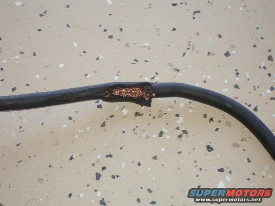 Close-up of a damaged black wire with exposed copper strands on a speckled floor