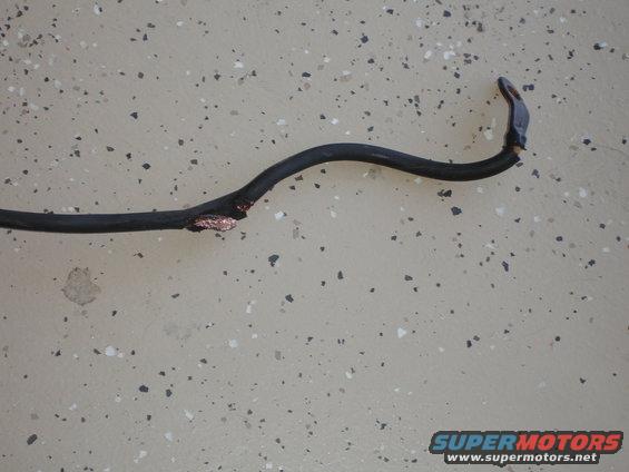 Damaged black electrical wire with exposed copper, lying on a speckled floor